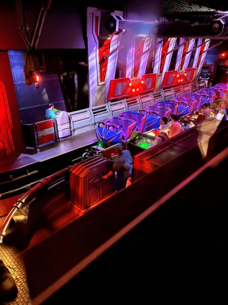 Guests board a futuristic roller coaster with purple seats and red lighting.