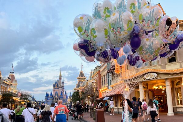 Adults enjoy Magic Kingdom with balloons and Cinderella Castle at dusk.