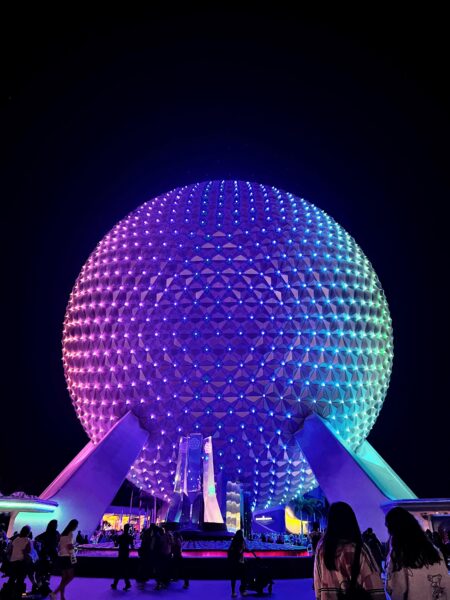 Spaceship Earth at Epcot lit up with colorful lights at night, a popular Disney World attraction.