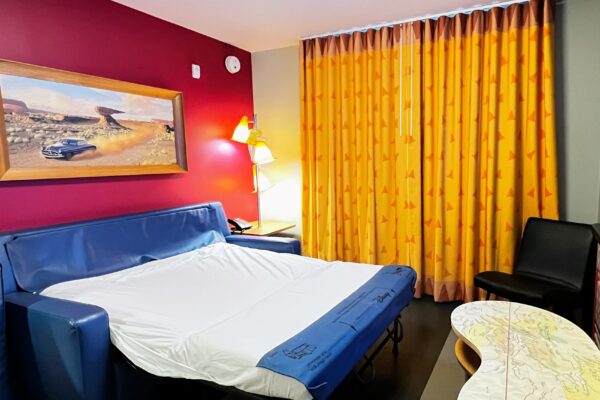 Disney hotel room with queen sofa bed, art, and yellow curtains.