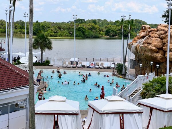 Disney resort pool with guests enjoying a sunny day, a waterfall feature, and lush greenery.
