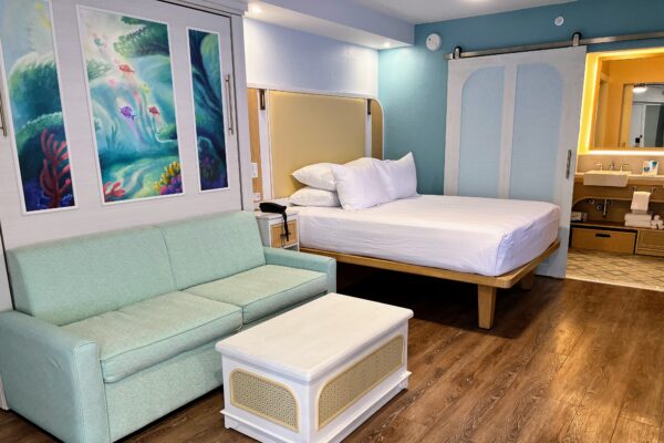 Disney room with queen bed, sofa, and mermaid art, suitable for adults.