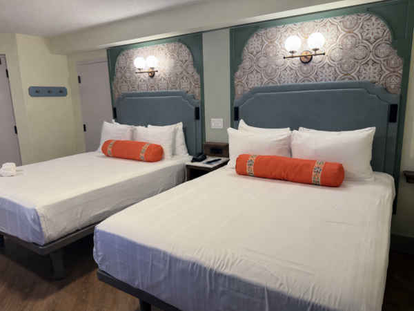 Disney resort room with two queen beds, orange bolster pillows, and decorative headboards.
