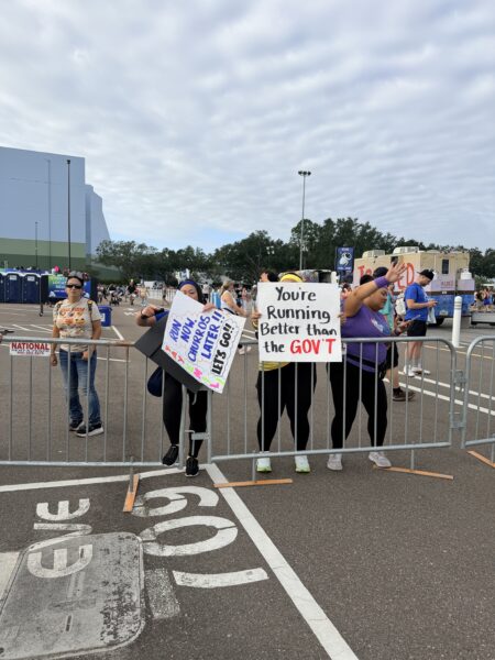 runDisney fans hold signs: "Run Churros Later!!" and "You're Running Better than the GOVT