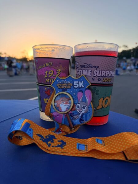 runDisney 5K medal and two souvenir race cups on a table at sunrise